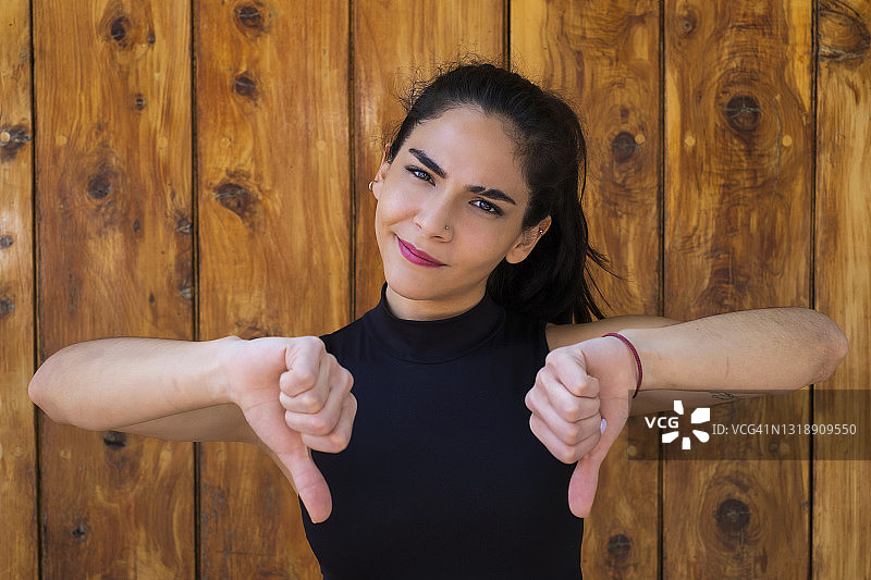 年轻的拉丁裔女人看着镜头，竖起大拇指向下图片素材