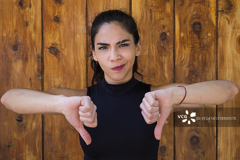 年轻的拉丁裔女人看着镜头，竖起大拇指向下图片素材