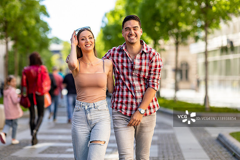 一对游客在阳光明媚的日子里在城市街道人行道上散步图片素材