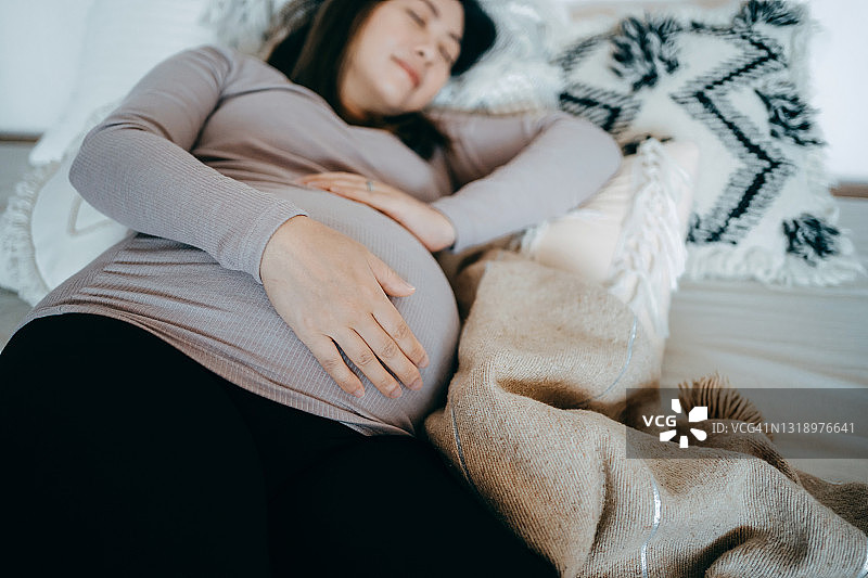 亚洲孕妇手捧腹部在床上睡觉，孕期舒适睡姿，失眠、睡眠障碍和身体不适图片素材