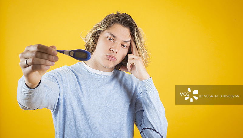 黄色背景下手持温度计的长发年轻男人图片素材