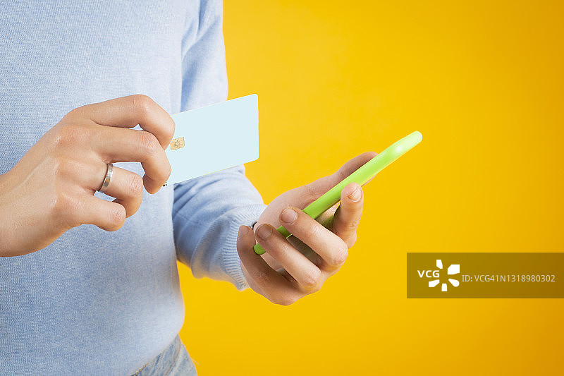 拿着信用卡和智能手机的金发男人（黄色背景）图片素材
