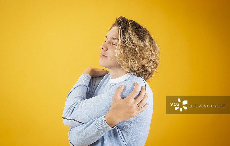 闭着眼睛放松的英俊长发男子拥抱自己图片素材