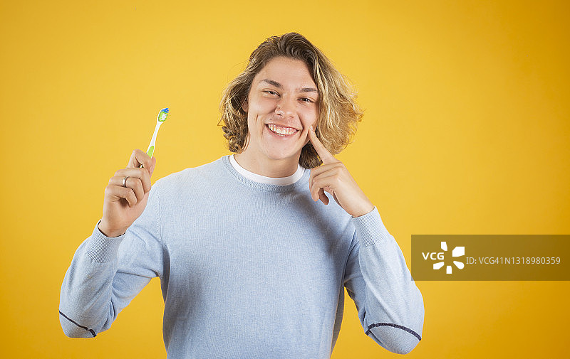 手持牙刷的金发男人，黄色背景图片素材
