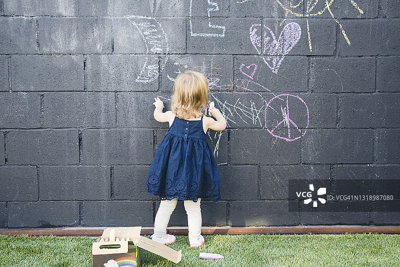在后院墙上用粉笔画画的小女孩背影图片素材