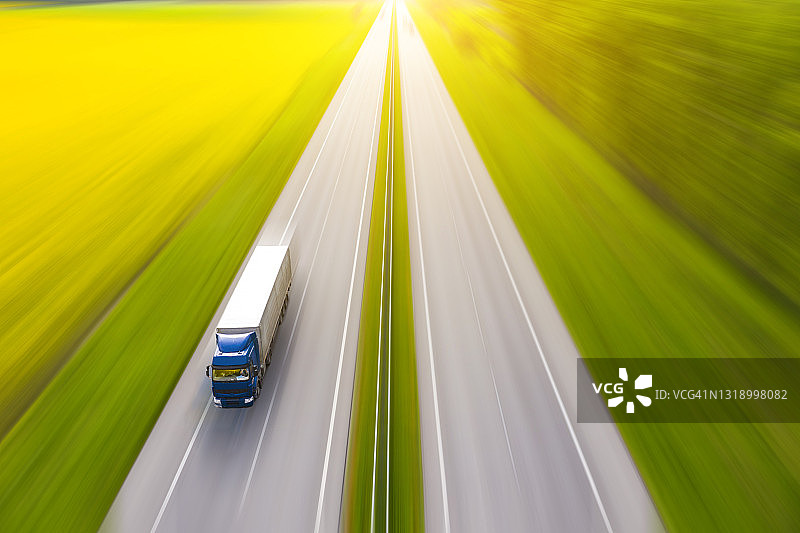乡村绿色田野中卡车在沥青路上行驶的航拍景色图片素材