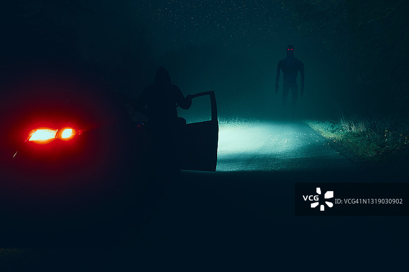 在雾蒙蒙的冬夜，男人在空旷的乡村道路上看着汽车旁的怪物外星人图片素材