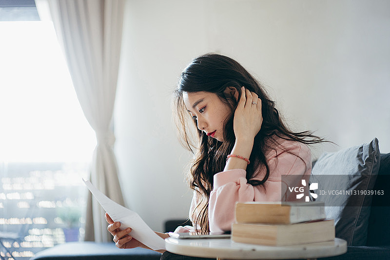 亚洲年轻女子在家用智能手机理财图片素材
