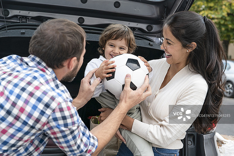 笑容满面的父亲在车外将运动球递给儿子图片素材