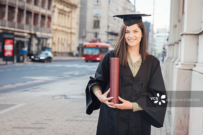 手持毕业证书站在大学前的漂亮毕业生图片素材