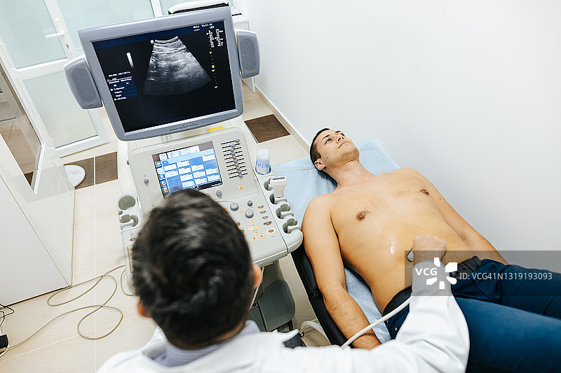 年轻男患者在医疗诊所接受腹部超声检查图片素材