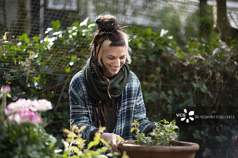 年轻女人对着她种在赤陶花盆里的植物微笑图片素材