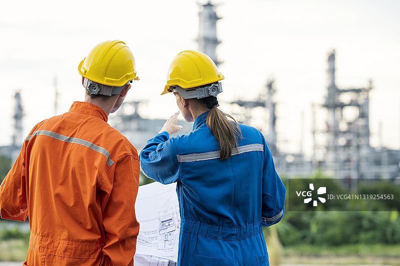 穿安全工作服的石油化工工程师讨论石油和天然气生产性能的背影。油气工业概念。图片素材