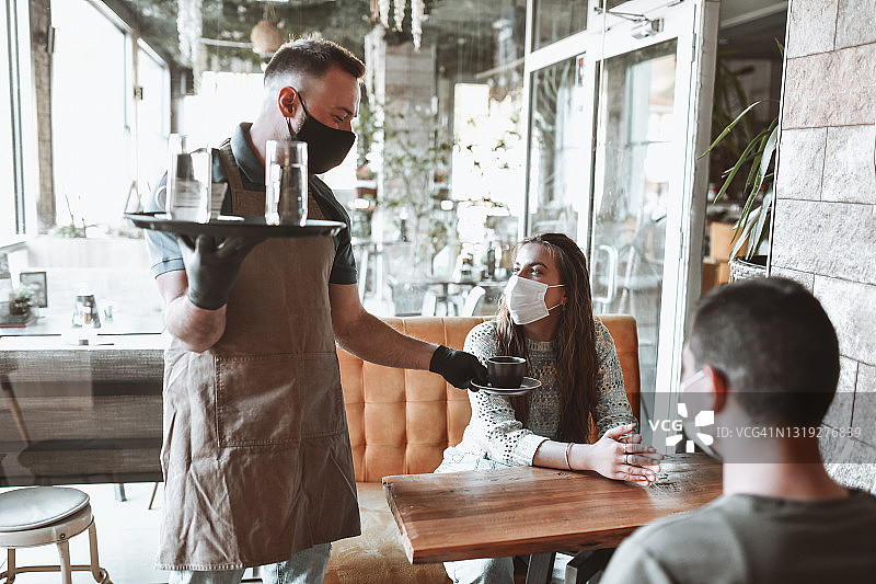 戴着口罩的情侣在咖啡吧从服务员那里接过咖啡和茶点图片素材