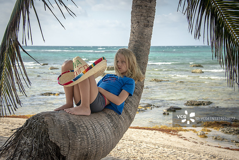 男孩戴着墨西哥帽躺在墨西哥卡门海滩的棕榈树上图片素材