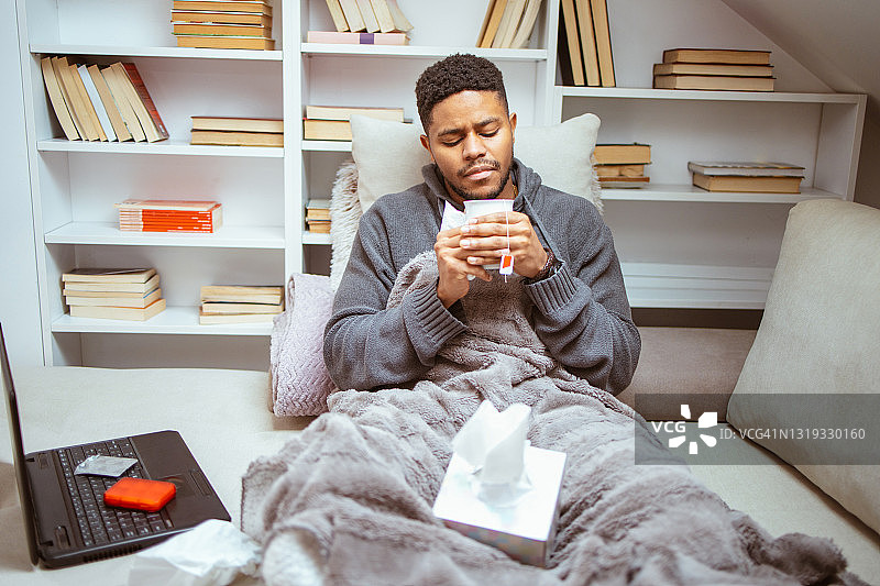 感冒卧床，用手帕擦鼻子的年轻非裔美国男子图片素材