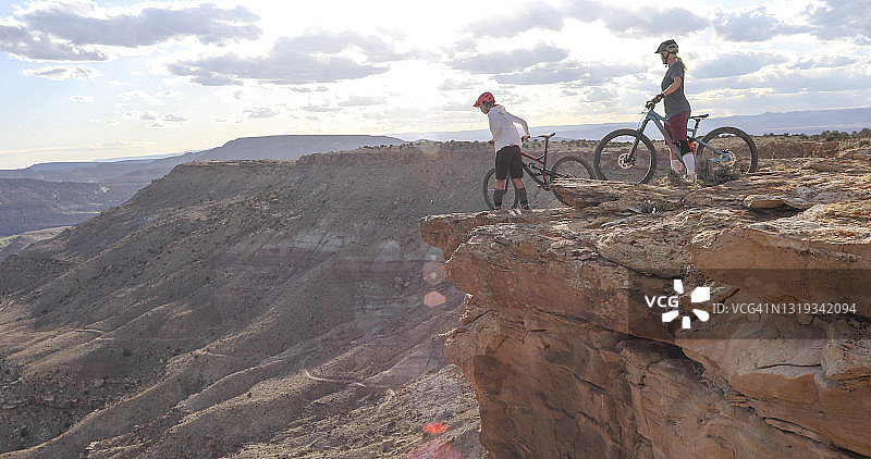 登山自行车手在悬崖边俯瞰峡谷和河流图片素材