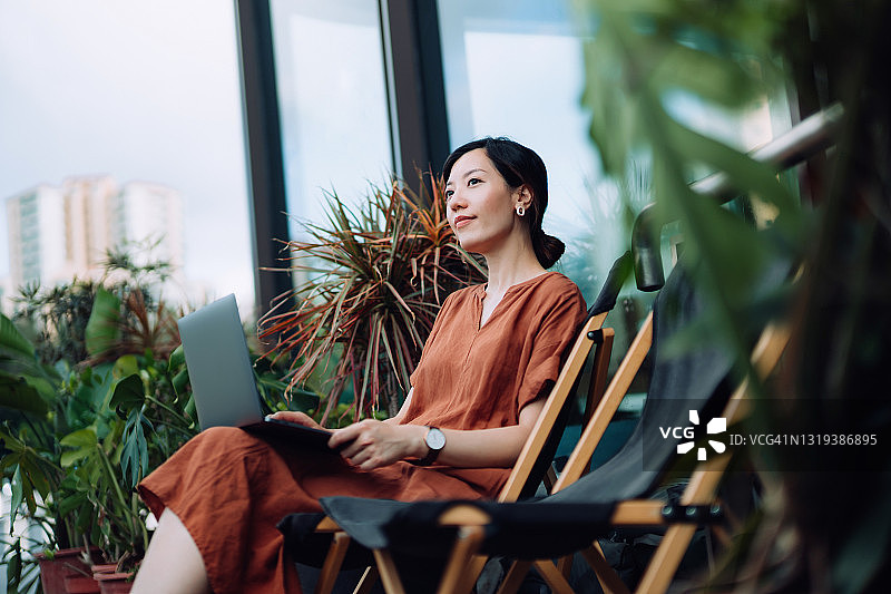年轻亚裔女性在后院躺椅上使用笔记本电脑，思考着图片素材