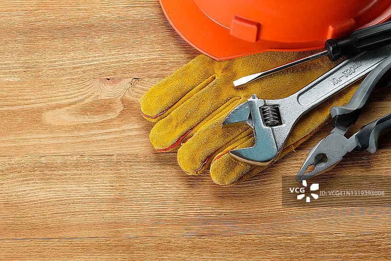 房屋建造或公寓维修工具，木质背景或桌子。工头的工作场所。家庭和专业维修、商业和建筑行业主题。防护手套、安全帽、钳子、螺丝刀和扳手。图片素材