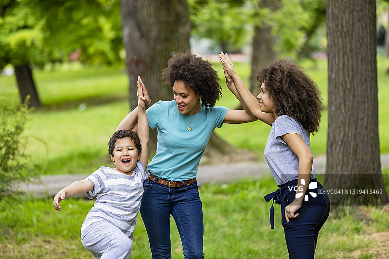 阳光明媚的日子里，年轻的非洲母亲和儿子女儿在公共场所散步图片素材