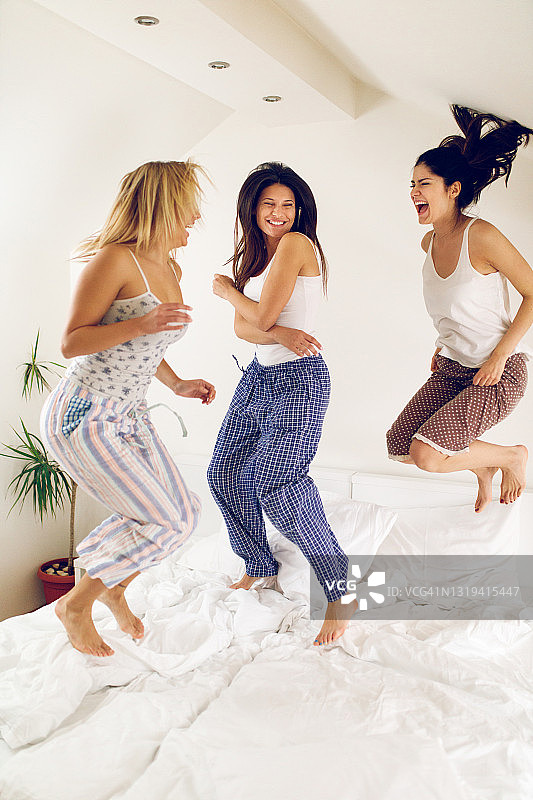 在睡衣派对上在床上跳跃嬉戏的女人图片素材