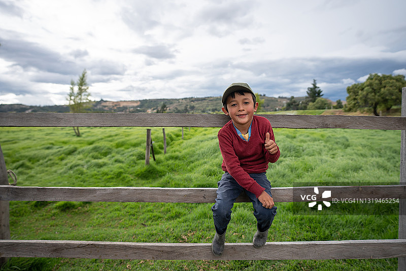 快乐的男孩坐在农场的栅栏上竖起大拇指图片素材