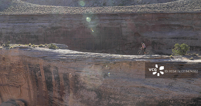 年轻女人骑山地自行车在峡谷上方的狭窄山脊上行驶图片素材