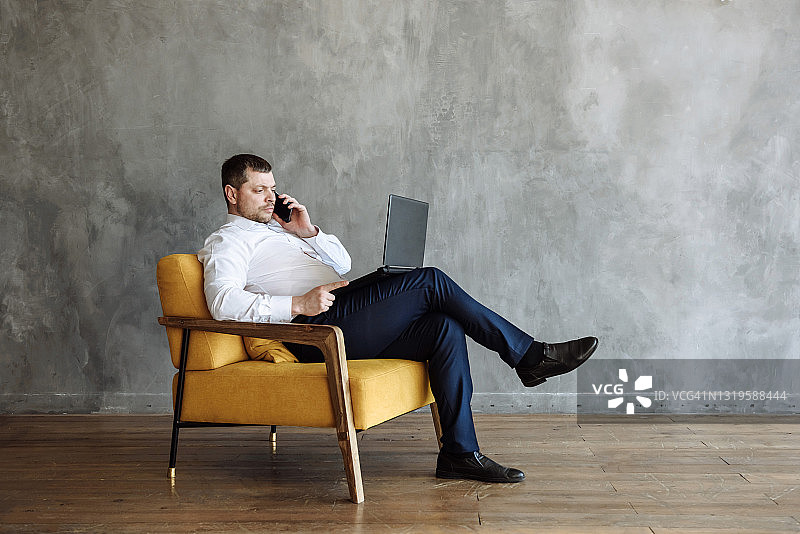 成年男人坐在椅子上使用笔记本电脑通话图片素材
