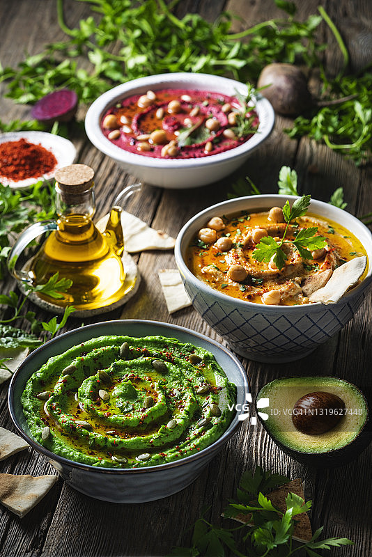 鹰嘴豆泥：三碗鹰嘴豆、鳄梨和甜菜根蔬菜，用于在乡村木桌上蘸酱图片素材