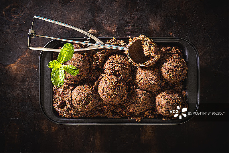 冰淇淋托盘中的巧克力冰淇淋球和深色木头上的薄荷叶图片素材