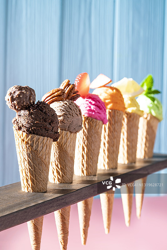 一排什锦冰淇淋蛋卷，粉色和蓝色木纹背景图片素材