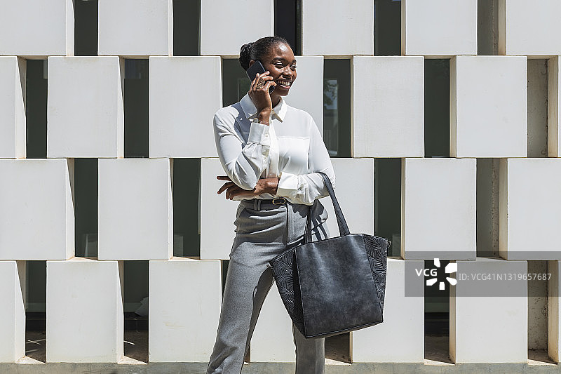 在积木墙前用手机交谈的微笑女企业家图片素材