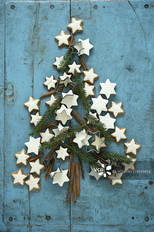 肉桂和针叶树枝在蓝色乡村木质背景上排列成圣诞树的圣诞肉桂星形饼干图片素材