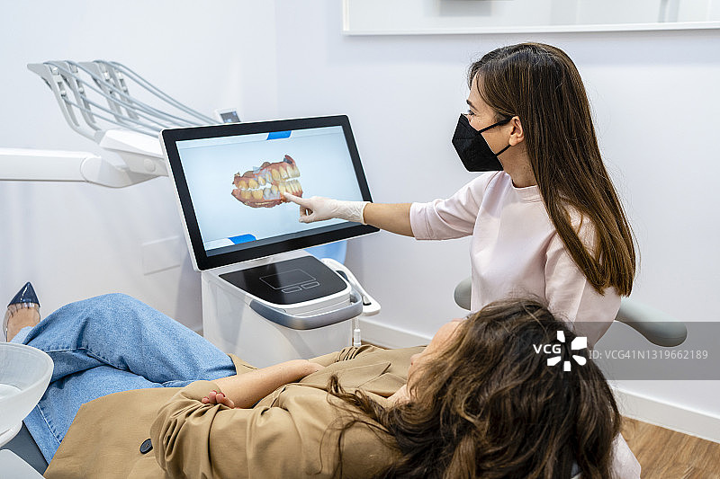 疫情期间，女牙医在诊所通过电脑屏幕向患者讲解图片素材