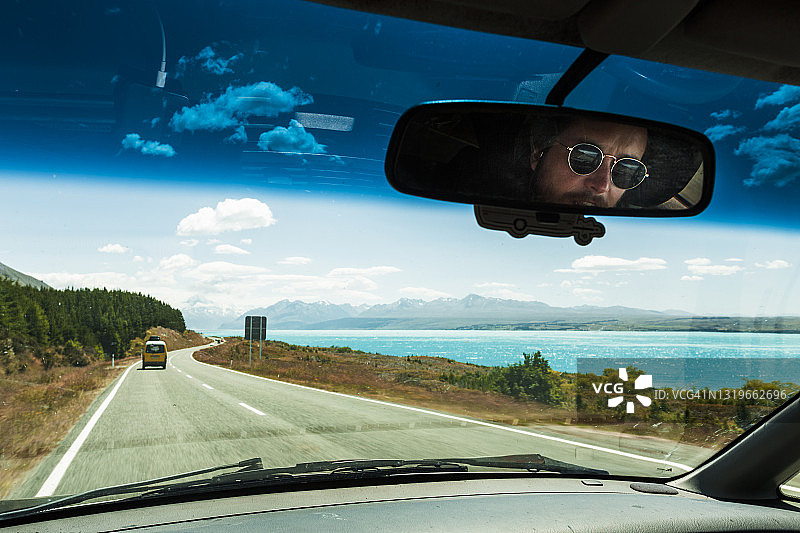 后视镜中男人驾车沿湖公路的倒影图片素材