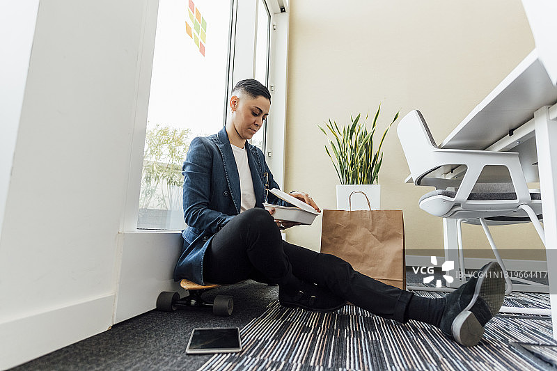 女企业家坐在办公室的滑板上打开食品盒图片素材