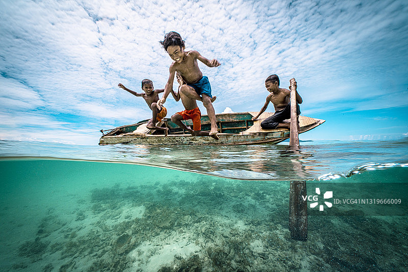 巴瑶族儿童在热带岛屿海滩的木制独木舟上跳跃图片素材
