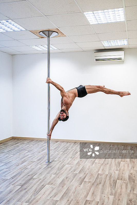 在杆子上保持平衡的健壮男性杂技演员图片素材