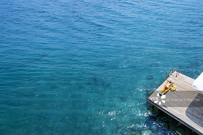 美丽的女人在海上木制码头上独自日光浴航拍照片图片素材