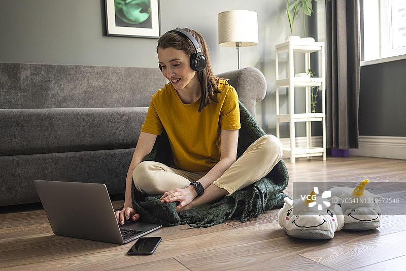 戴耳机的女人在家使用笔记本电脑工作图片素材