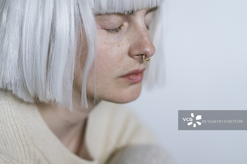 在白墙边闭着眼睛的时尚女性图片素材