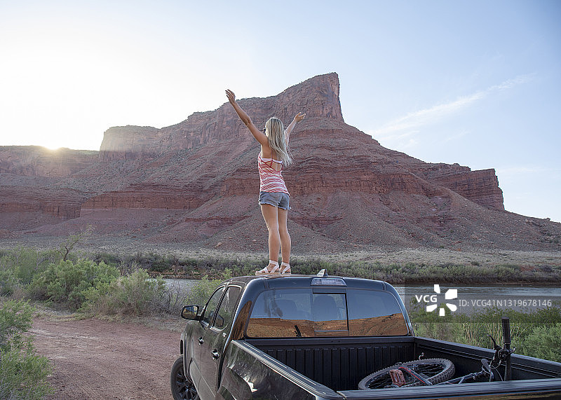 年轻女子在日出时分于皮卡车顶放松图片素材