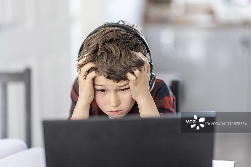 在家通过笔记本电脑上远程课程的疲惫男孩图片素材