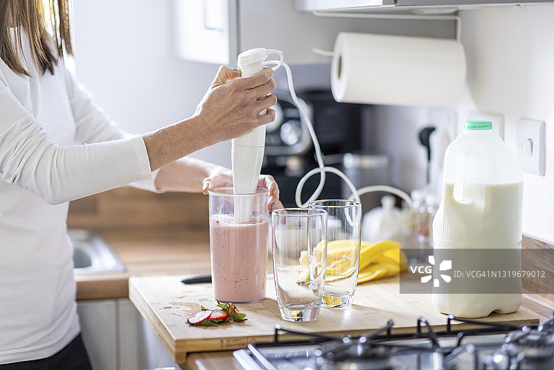 女人在厨房用玻璃杯准备草莓奶昔图片素材
