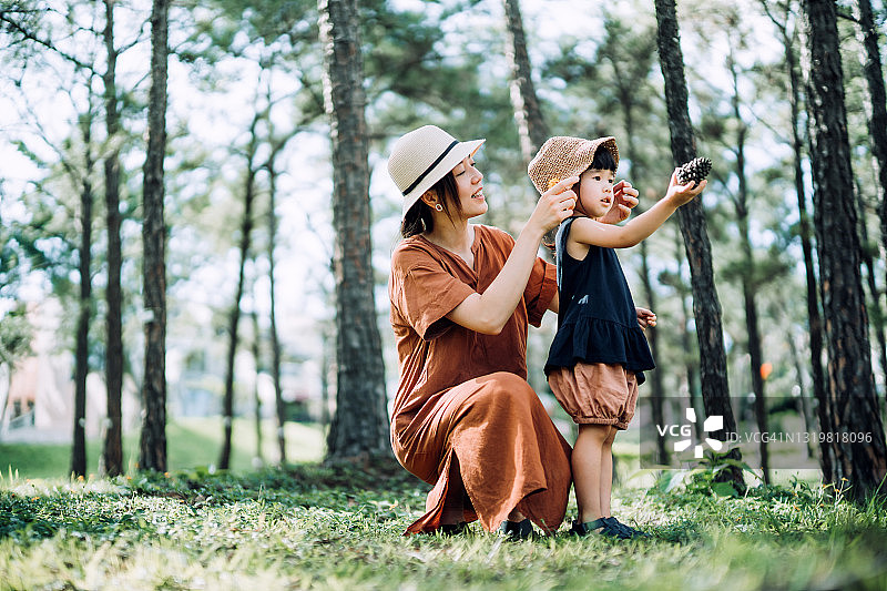 亚裔母亲为女儿戴草帽，享受阳光下的亲子时光图片素材