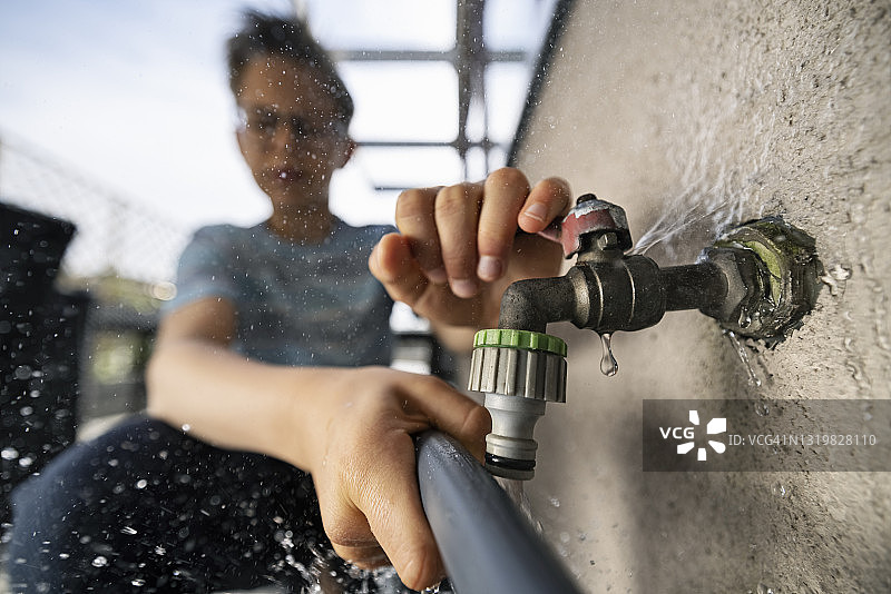 少年用坏水龙头给喷壶装水图片素材