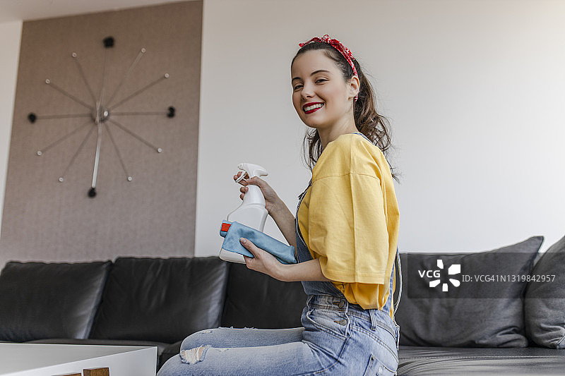 快乐的年轻女人用喷雾和抹布打扫房子图片素材