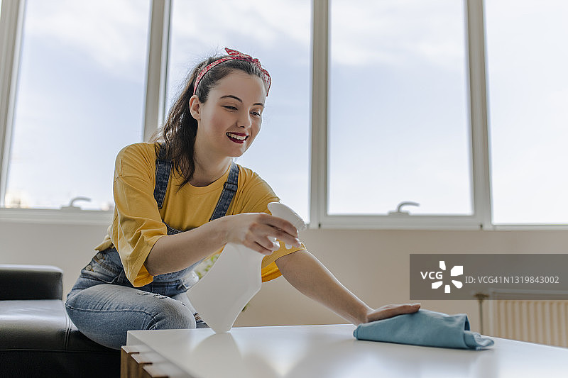 快乐的年轻女人用喷雾和抹布打扫房子图片素材