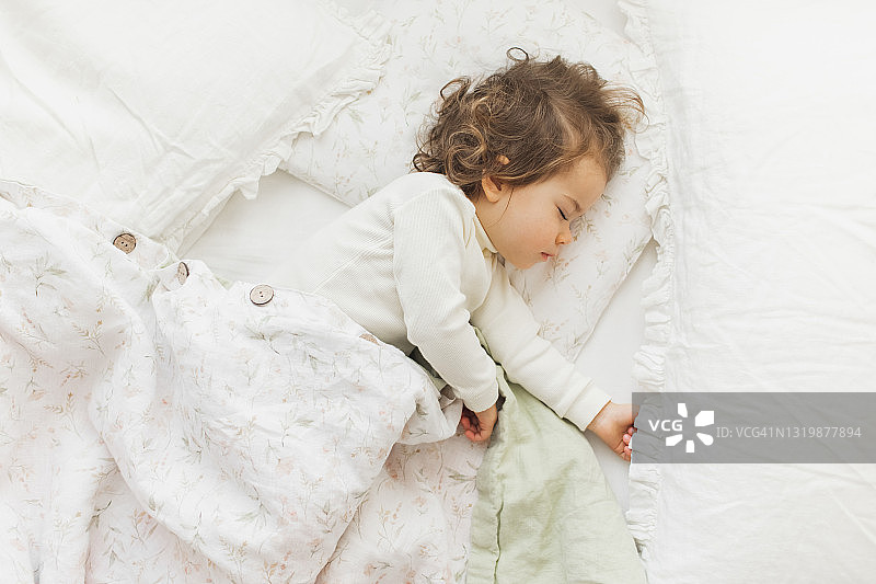 在阳光明媚的育儿室里，躺在亚麻毯子下睡觉的可爱女婴图片素材