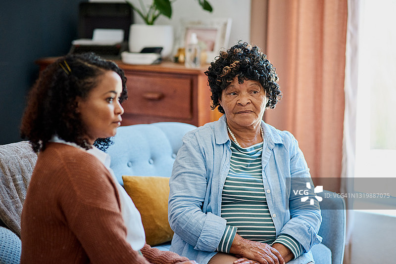 老年妇女和女儿坐在家中的沙发上，没有交谈图片素材